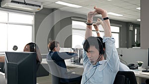 Call center is tired, young adult employee working with headset stretch while working hard
