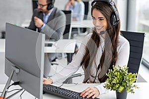 Call center worker accompanied by her team working with a headset at office