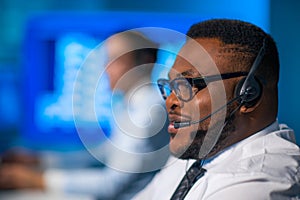 Call-center worker is speaking with the client by headset. Workplace of the african-american support operator.