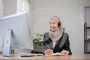 Call center worker, young Muslim woman wearing hijab, talking to customer on call phone on computer in customer service