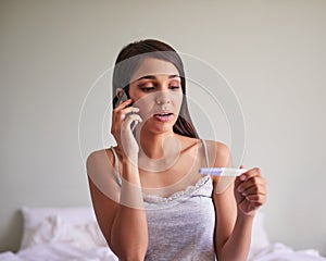 On the call with her husband waiting for the results. an attractive young woman taking a pregnancy test at home.