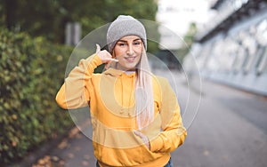 Call me. Woman gesturing at speaking on phone while looking to camera. Outdoors daylight. Woman on phone