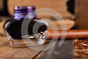 Calligraphy nib and ink in inkwell on a wooden table. Writing accessories in the old workshop