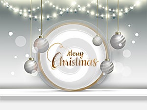 Calligraphy text Merry Christmas in circular frame with hanging baubles and lighting garlands.