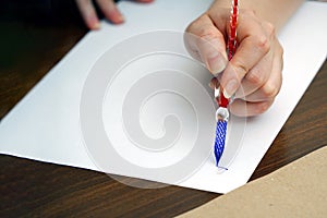 Calligraphy training. A woman& x27;s hand holds a glass feather with blue ink and begins to write on a piece of paper.