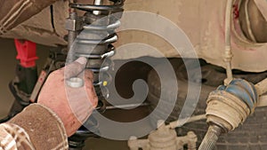 The calloused hands of a mechanic twist the coil spring ties with a wrench during DIY car repairs.