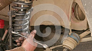 The calloused hands of a mechanic twist the coil spring ties with a wrench during DIY car repairs.