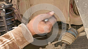 The calloused hands of a mechanic twist the coil spring ties with a wrench during DIY car repairs.