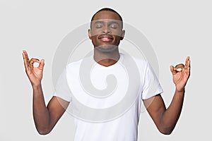 Calm African American man meditating, practicing yoga with closed eyes
