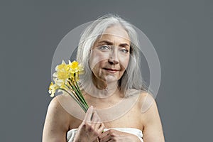 Calm aged european lady with gray hair hold bouquet of yellow flowers, enjoy spring, freshness