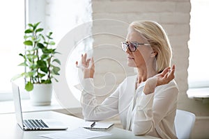 Calm aged woman meditate with mudra hands in office