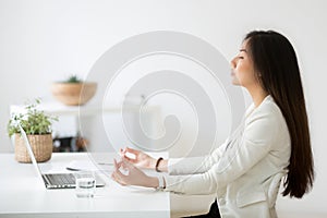 Calm Asian employee meditating in office relieving work stress