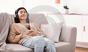 Calm asian woman listening to music wearing headphones