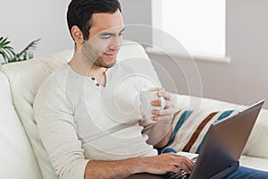 Calm attractive man drinking coffee while working on his laptop