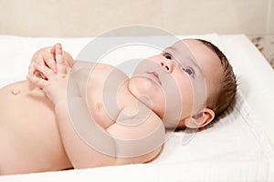Calm baby boy lying on his back with crossed fingers on table for nappy changing, enjoying time
