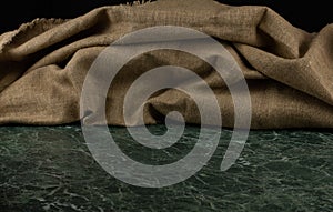 Calm background. On a green marble table lies a pile of beige linen or burlap. The beautiful texture of the fabric forms