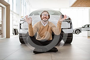 Calm bearded man sitting at lotus pose near new bought car.