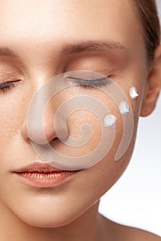 Calm beautiful woman with closed eyes applying cream anti aging care, cosmetology treatment.