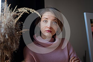 Calm beautiful woman standing near a bouquet of spikelets and looking at the camera. Blonde girl with short hair wearing