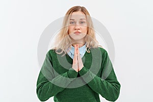 Calm beautiful young woman showing pray, namaste gesture, express gratitude, thank you sign, standing in green sweater over white