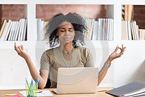 Calm black businesswoman taking break meditating doing yoga at work photo