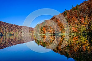 Calm blue lake with reflections of hills and forest in intense fall colors