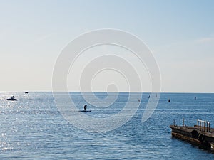 Calm blue sea with boats and surfers in it under clear skies