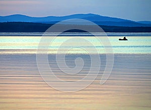 Calm blue sunset sky over the lake, silhouette of a lone boat with a fisherman, calm surface of water, lake Uvildy photo