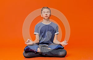 Calm boy sitting on floor and meditating in lotus position.