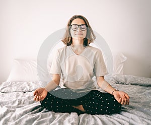 Calm brunette curly young woman doing yoga relaxing on bed at home in bedroom