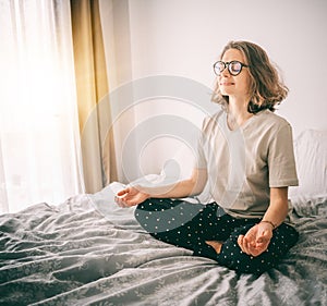 Calm brunette curly young woman doing yoga relaxing on bed at home in bedroom