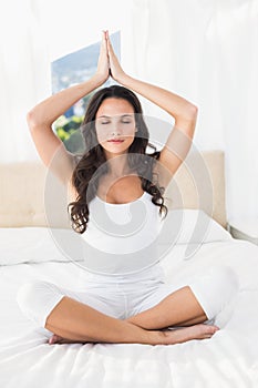 Calm brunette doing yoga on bed