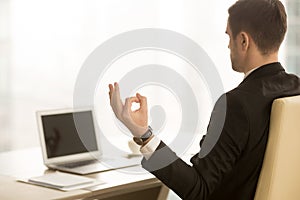 Calm businessman meditating in workplace, chin mudra, yoga at wo