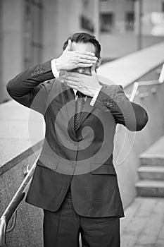 Calm businessman standing near of office with hands covering his mouth and eyes