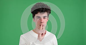 Calm caucasian man shh gesturing against green background