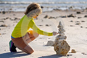 Calm child play with pyramid stones balance on the sand of summer beach. Child play with stack of stones. Child play on