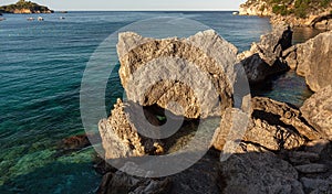 Calm clear green sea at shore with large rocks, sun shines to small waves, typical scenery at one of many bays in Liapades, Greece