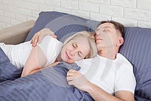 Calm couple sleeping and spooning in bed in bedroom at home.