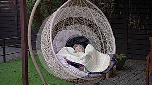 Calm cute baby girl sleeping in hanging chair in patio on backyard outdoors. Wide shot portrait of Caucasian toddler