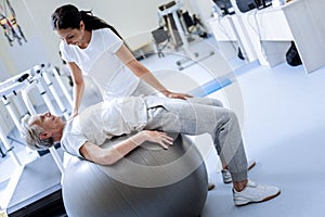Calm doctor persuading her patient to relax while being on a fitball
