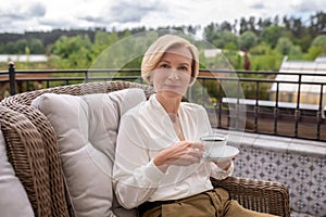 Calm elegant blonde woman drinking coffee outdoors