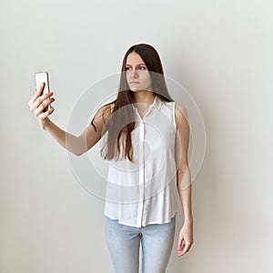 Calm, emotionless woman takes selfie on cell phone. Serious, unflappable female