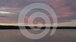 Calm evening by the lake with burning sky and forest in the background. Colourful sunset sky by the water shore. Peaceful time