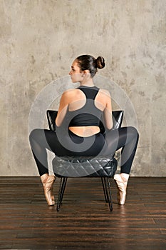 Calm feminine ballerina sitting on chair during rehearsal