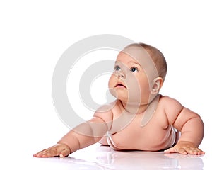 Calm and focused infant child baby girl kid in diaper is lying on her tummy holding arm outstretched and looking up
