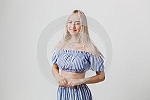 Calm and friendly beautiful blonde girl in summer outfit is smiling posing at camera, over white background. Emotions