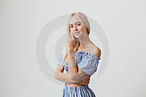 Calm and friendly beautiful blonde girl in summer outfit is smiling posing at camera, over white background. Emotions
