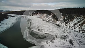 Calm, frozen river covered with ice on cold winter day. Peaceful river water and snowy coast on cold gray day in winter