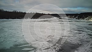 Calm, frozen river covered with ice on cold winter day. Peaceful river water and snowy coast on cold gray day in winter