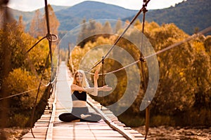 Calm girl practicing yoga meditation sitting in lotus pose on bridge over mountain river. Wellbeing Concept.